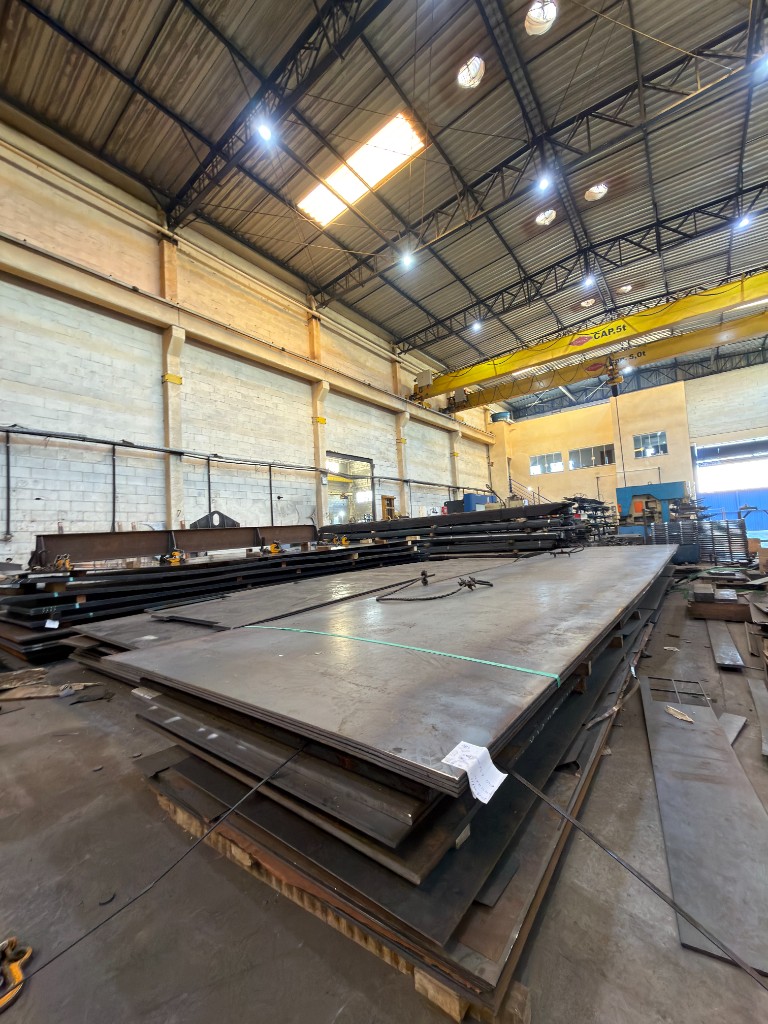 Estoque de chapas de aço empilhadas no galpão industrial da SteelForte com ponte rolante de 5 toneladas